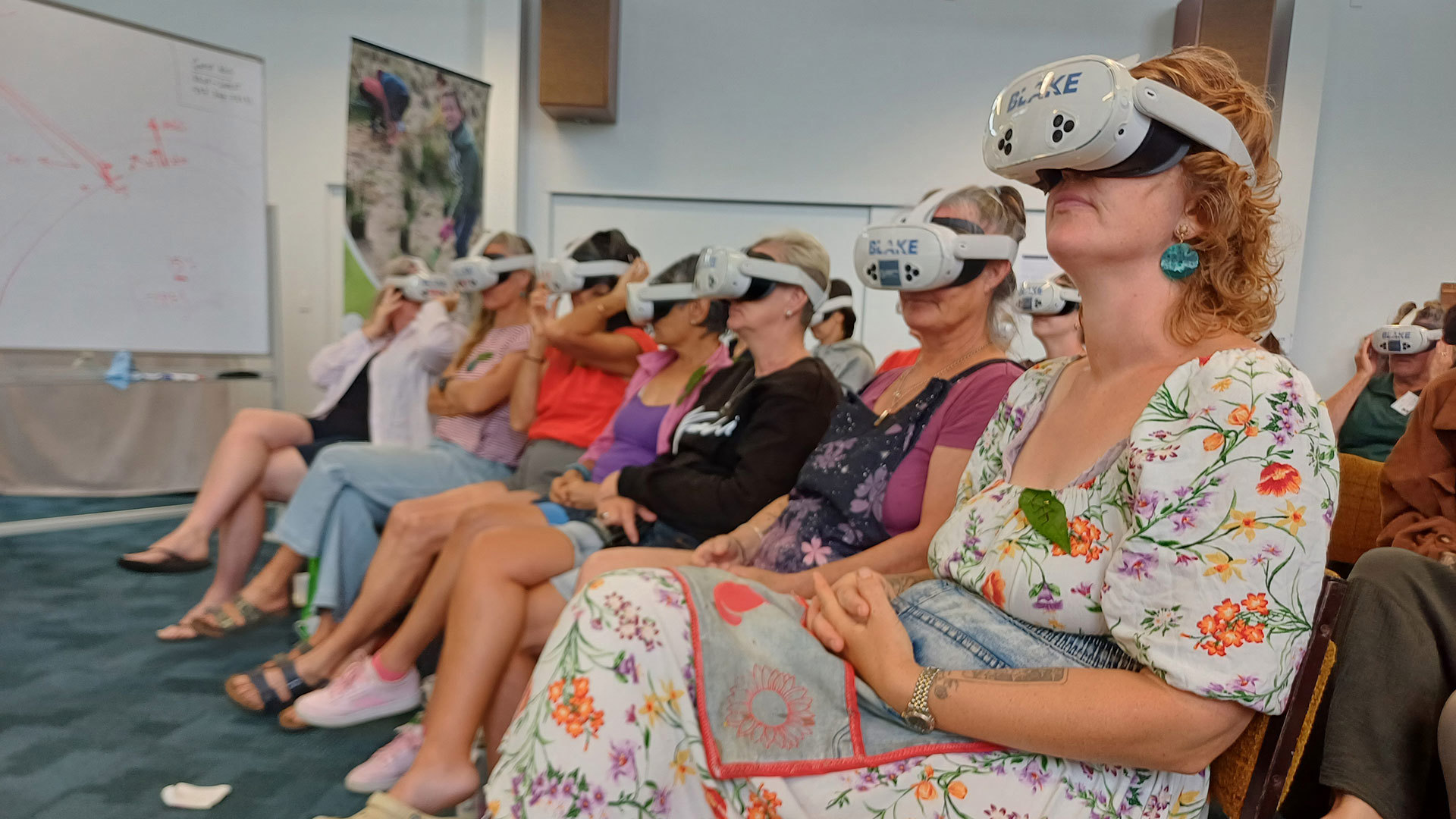Several women in a row seated on chairs wearing virtual reality headsets.