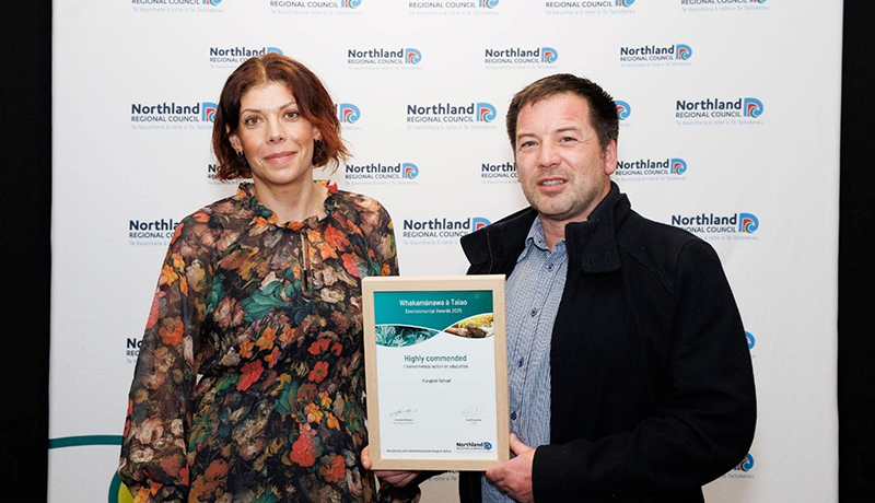 Man and woman with certificate in front of Northland Regional Council logo backdrop. (Photo: Dawn Dutton Photography).