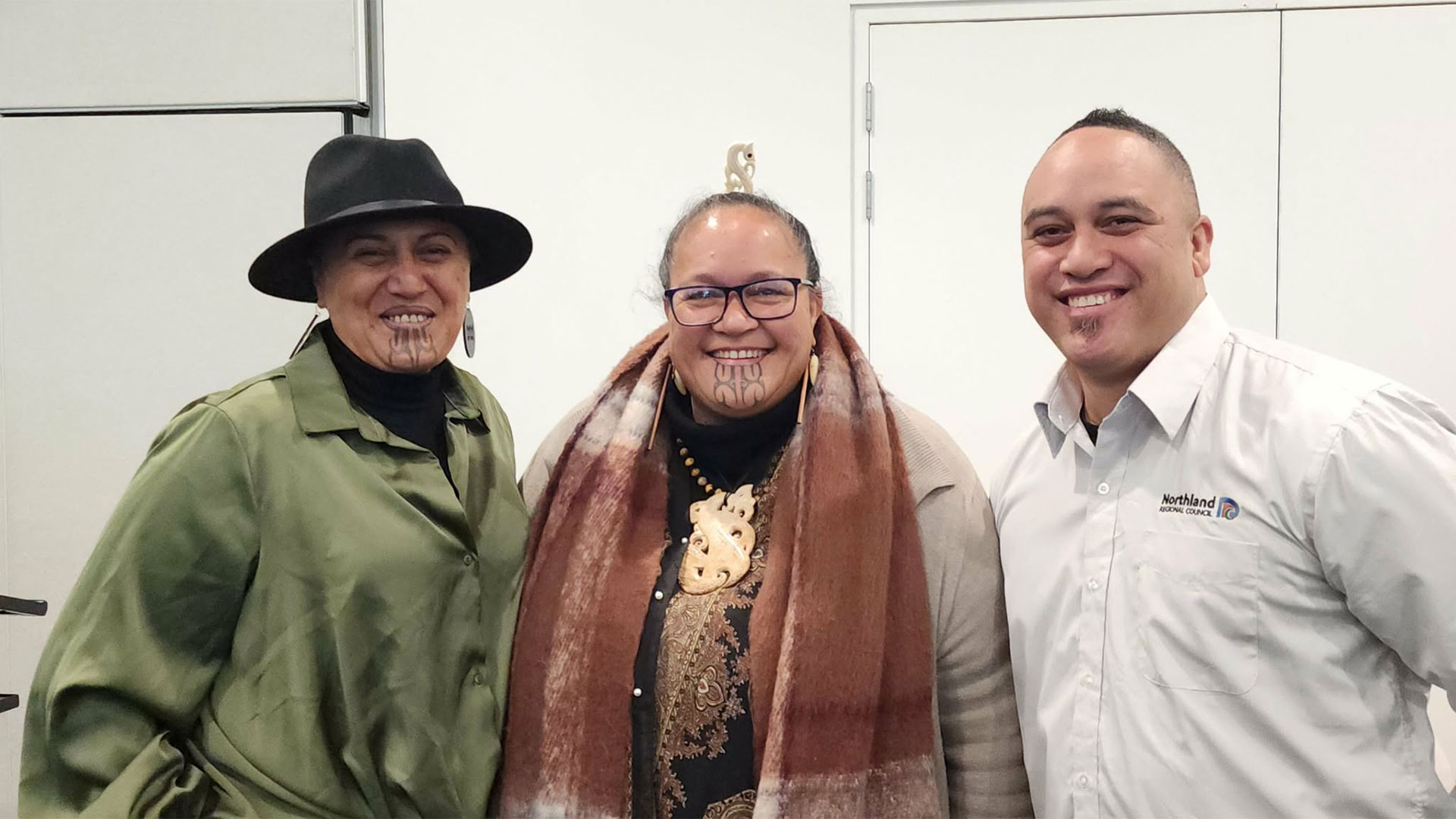 A woman wearing a hat, another wearing a scarf and a man stand together.