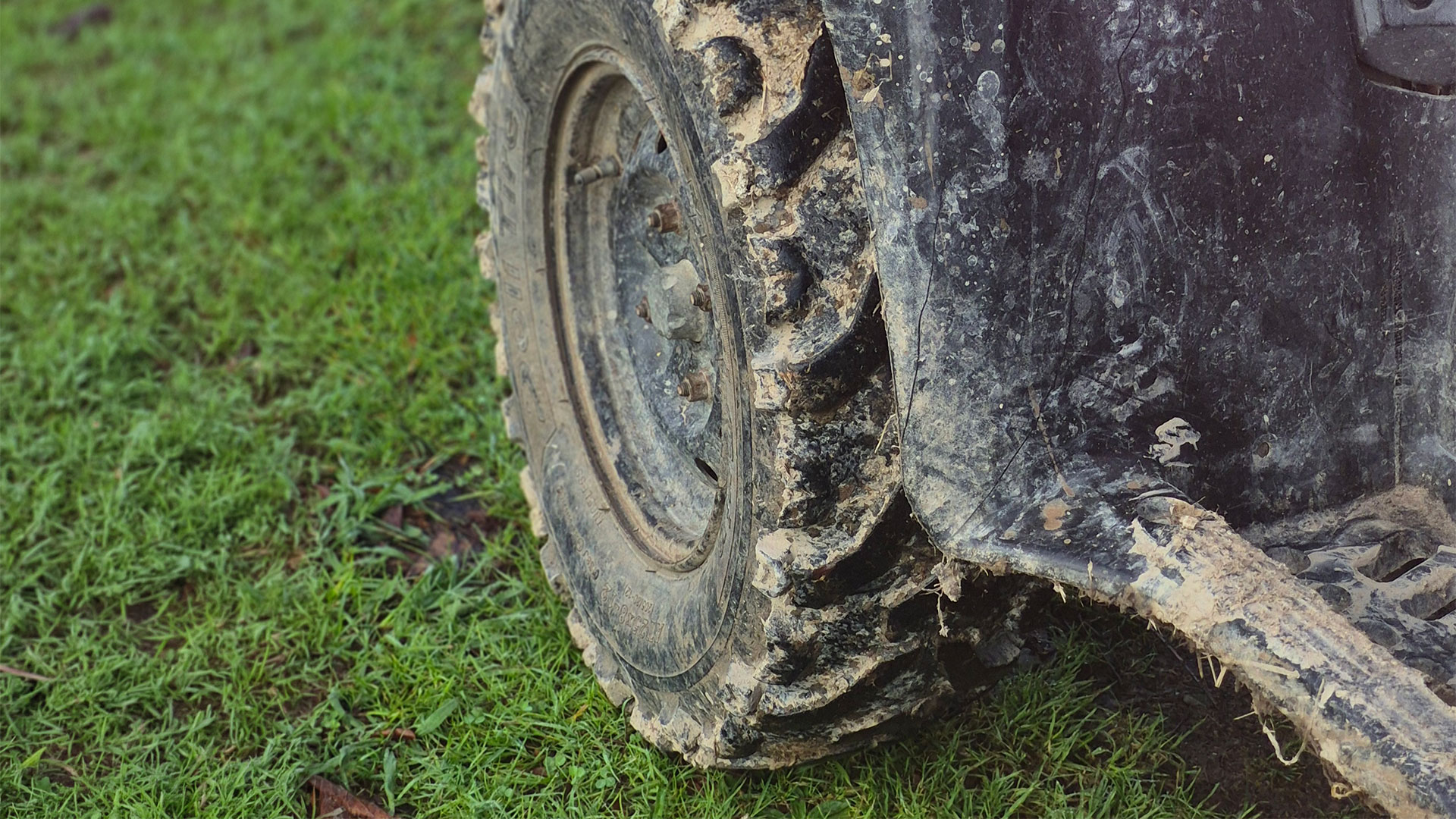 Grass, muddy wheel and guard of a quad bike.