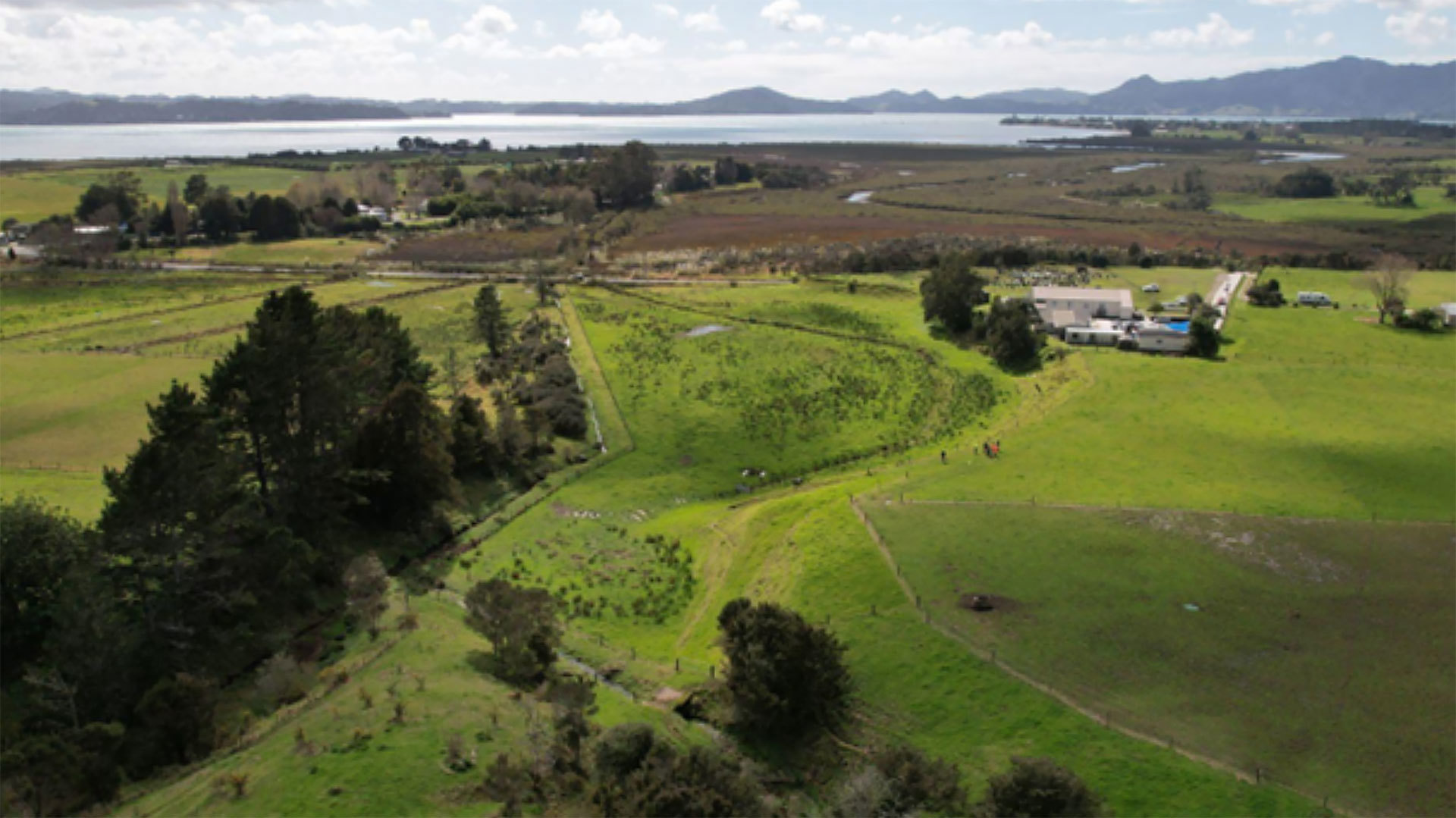 Aerial view of rural countryside with harbour and hills in the background.