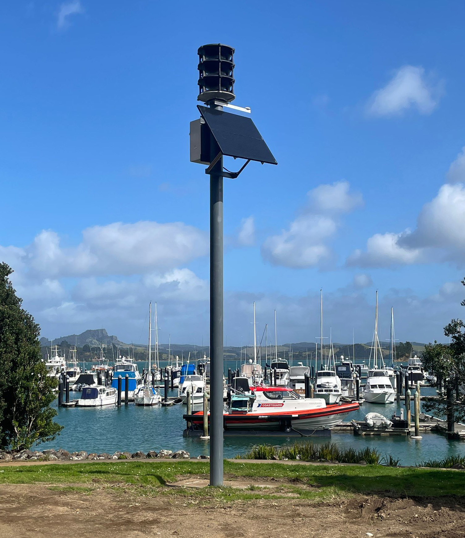 A solar powered siren on top of a pole in front of boats in a marina