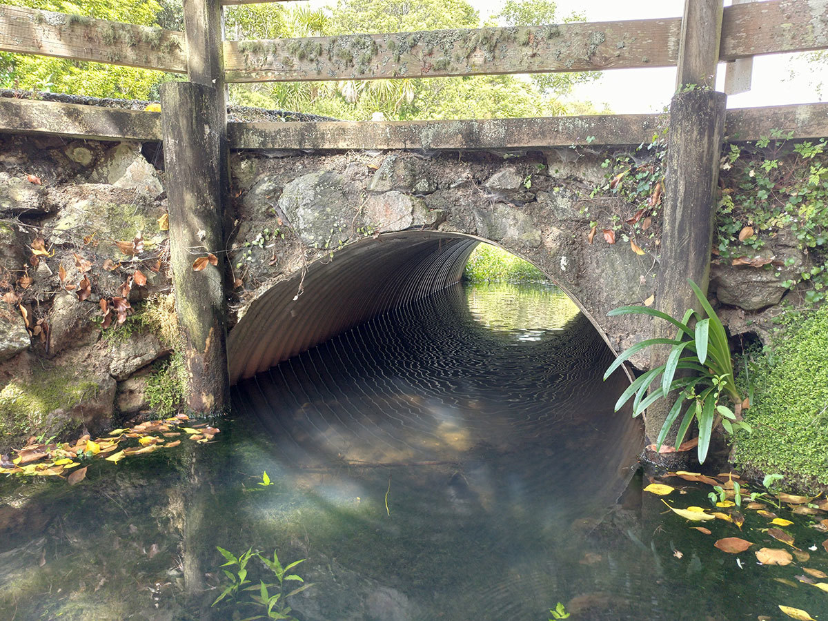 Water flowing through a culvert under a bridge.