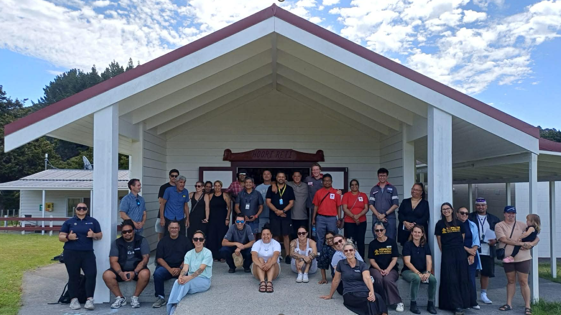 Group of people with some standing others sitting in front of the entrance to the marae.