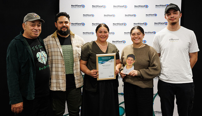 Three men and two women (one holding a photograph of a young man) with a certificate in front of Northland Regional Council logo backdrop. (Photo: Dawn Dutton Photography).