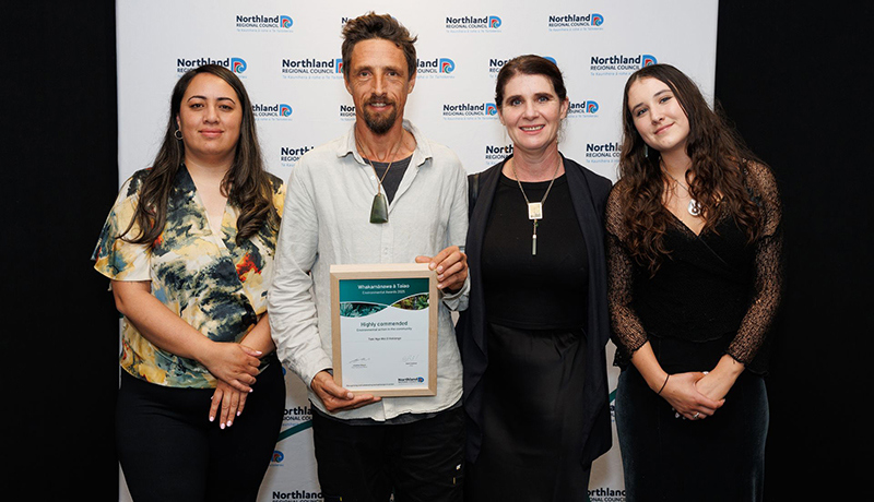 Three women with a man in the centre holding a certificate in front of Northland Regional Council logo backdrop. (Photo: Dawn Dutton Photography).
