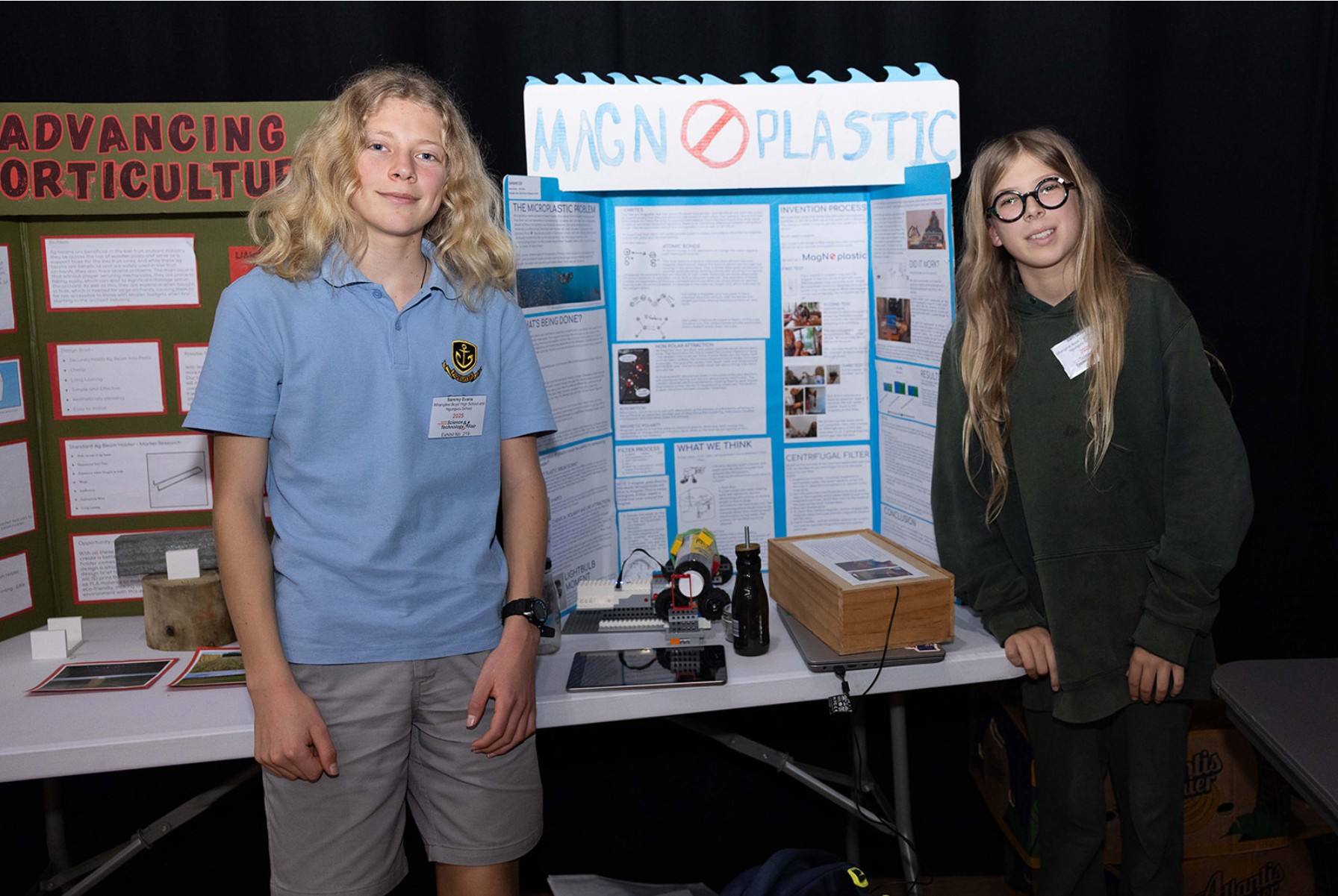 Two students stand beside a science fair display about reducing microplastic pollution.